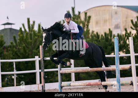 Sautez sur la barrière. Jeune fille sportive, entraînement des adolescents à l'arène d'équitation en été, en plein air. Dressage de chevaux. Équitation. Modèle dans le sport Banque D'Images