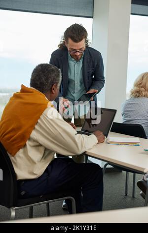 Young hipster educator teaching group of senior multiracial people using technology and the internet in the classroom. Stock Photo