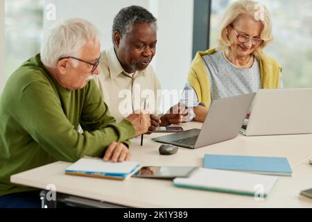 A cheerful multicultural group of senior students is doing an assignment on laptops in the classroom. Stock Photo