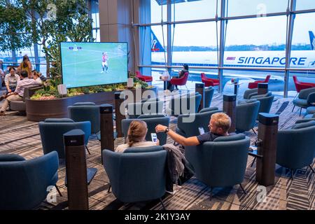 Passagers regardant la télévision dans le salon en attendant le vol. Aéroport international de Changi Singapour Banque D'Images