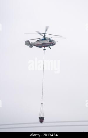 Un hélicoptère d'incendie transporte un conteneur d'eau pour éteindre un incendie dans un bâtiment de production Banque D'Images