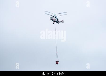 Un hélicoptère d'incendie transporte un conteneur d'eau pour éteindre un incendie dans un bâtiment de production Banque D'Images