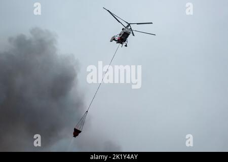 Un hélicoptère d'incendie transporte un conteneur d'eau pour éteindre un incendie dans un bâtiment de production Banque D'Images