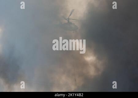 Un hélicoptère d'incendie transporte un conteneur d'eau pour éteindre un incendie dans un bâtiment de production Banque D'Images