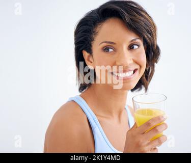 Rien de mieux qu'un verre de jus rafraîchissant. Une belle jeune femme appréciant un verre de jus d'orange frais. Banque D'Images