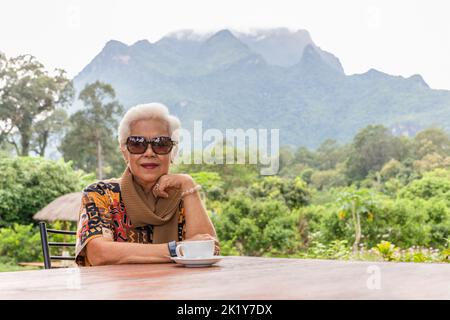 ASIN gris blanc cheveux femme senior boire un café dans un café extérieur avec vue sur la montagne. Banque D'Images