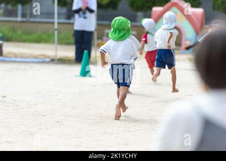 Les enfants qui s'exécutent sur le terrain pendant une journée de sport à une école maternelle japonaise Banque D'Images