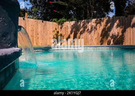 Vue rapprochée d'une piscine d'accent gris avec eau turquoise dans une cour clôturée dans un quartier de banlieue Banque D'Images