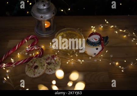 Photo de Noël chaleureuse. Tasses transparentes avec tranches de thé et de citron, bonhomme de neige souvenir, biscuits, guirlande lumineuse, sucettes, b Banque D'Images