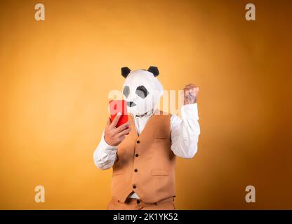 Homme en panda masque d'ours sur fond jaune à l'aide d'un smartphone. Banque D'Images