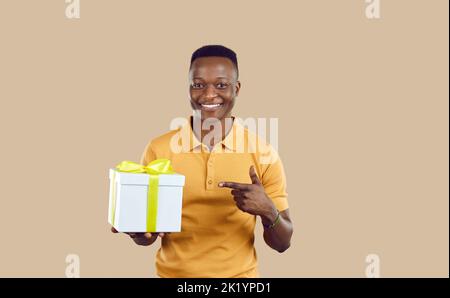 Joyeux jeune Afro-américain souriant et pointant vers le présent dans sa main Banque D'Images