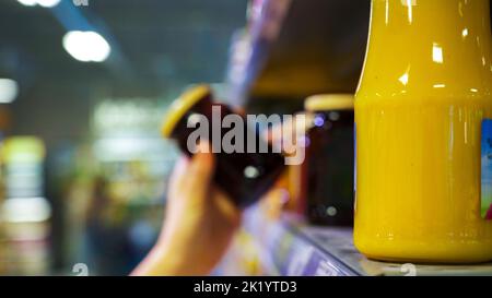 Arrière-plan flou: La main d'une femme prend un pot de verre de gelée de l'étagère. Banque D'Images