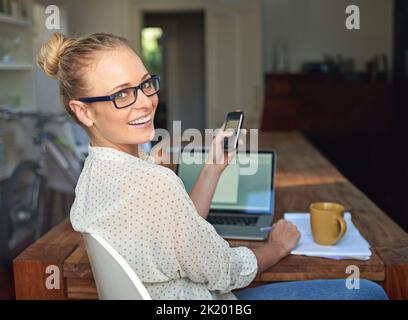 Travailler dans le confort de la maison. Une jeune femme utilisant son téléphone portable tout en travaillant de la maison. Banque D'Images