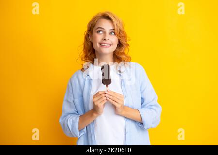 La jeune femme mange des crèmes glacées au chocolat sur fond jaune. Drôle femme de tête rouge avec de la crème glacée. Banque D'Images