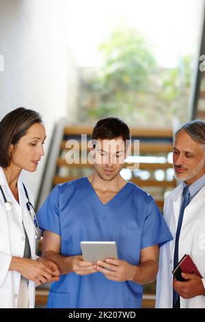 Accès rapide aux antécédents médicaux d'un patient. Un petit cliché d'un beau jeune médecin montrant des informations sur sa tablette à ses collègues Banque D'Images