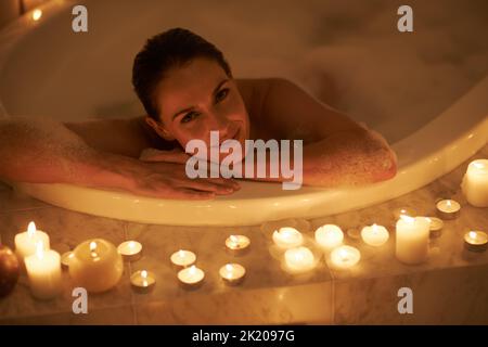 Rien ne se détend mieux qu'un bain moussant. Une femme magnifique se détendant dans une baignoire éclairée aux chandelles. Banque D'Images