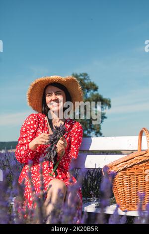 une jeune femme dans un chapeau de paille est assise sur un banc blanc dans un champ de lavande et porte une couronne Banque D'Images