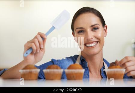 C'est le glaçage sur le gâteau. Une jeune femme heureuse sur le point d'appliquer sa glaçant sur son lot de petits gâteaux fraîchement cuits. Banque D'Images