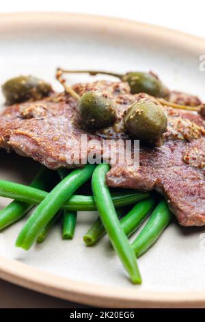 steak de porc avec sauce moutarde et câpres servi avec des haricots verts Banque D'Images