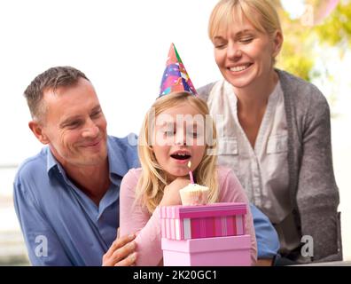 Faites un vœu. Une courte photo d'un couple heureux en regardant leur petite fille souffler une bougie sur son anniversaire Banque D'Images