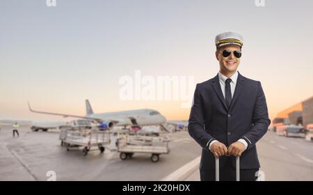 Jeune pilote debout avec une valise sur un aéroport avec un avion en arrière-plan Banque D'Images