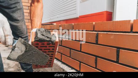 Le constructeur applique du mortier de ciment à la brique rouge de près. Concept de bâtiment en brique. Banque D'Images