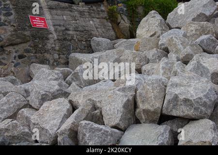 Armure de roche transportée à Coverack Bay, Cornwall. Renforcer le mur de la mer contre les dommages causés par les tempêtes et l'érosion. Signe ironique avertissant les piétons. Banque D'Images