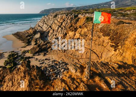Brandir le drapeau portugais plus de ciel bleu et l'océan, la plage de Guincho, Portugal Banque D'Images