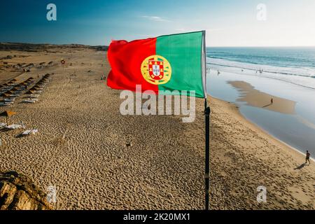 Brandir le drapeau portugais plus de ciel bleu et l'océan, la plage de Guincho, Portugal Banque D'Images