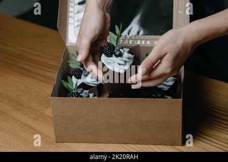 Gros plan des mains des femmes mettant un cupcake dans une boîte Banque D'Images