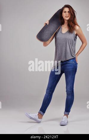 Le skateboard n'est pas un hobby, c'est un mode de vie. Portrait en studio complet d'une jeune femme vêtue de façon décontractée et tenant sur un skateboard Banque D'Images