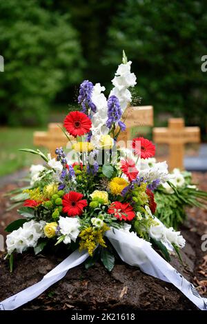 fleurs colorées comme arrangement grave après un enterrement devant des croix en bois dans un fond flou Banque D'Images