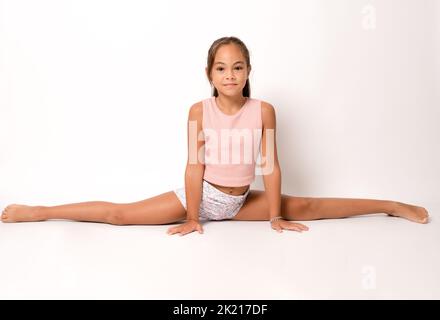 La gymnaste de fille d'enfant démontre la flexibilité ficelle assise isolée sur fond blanc. Banque D'Images