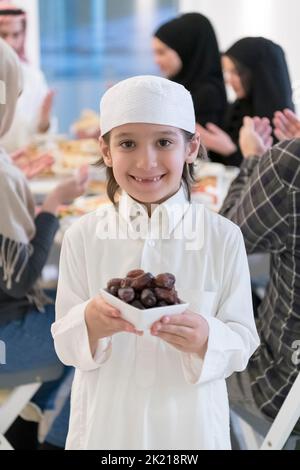 EID Mubarak famille musulmane ayant Iftar dîner petit garçon tenant une assiette pleine de dates sucrées pour briser la fête. Manger de la nourriture traditionnelle pendant le ramadan Banque D'Images