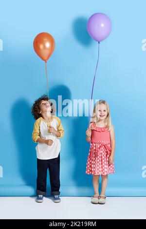 Pourquoi le mien ne va pas aussi haut que le mien. Une jolie petite fille et un garçon debout dans un studio tenant un ballon Banque D'Images