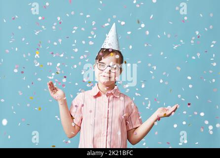 Taille vers le haut portrait pf fille ludique avec le syndrome de duvet appréciant la douche confetti à la fête sur fond bleu Banque D'Images