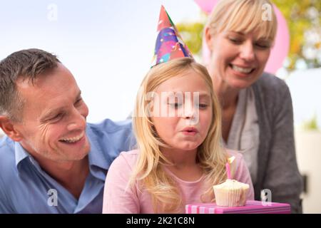 Un souhait pour la fille d'anniversaire. Une photo courte d'une petite fille heureuse et de ses parents célébrant son anniversaire Banque D'Images