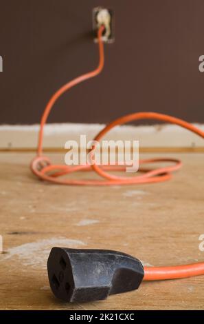 Rallonge électrique orange sur le sol en contreplaqué à l'intérieur de la maison. Banque D'Images