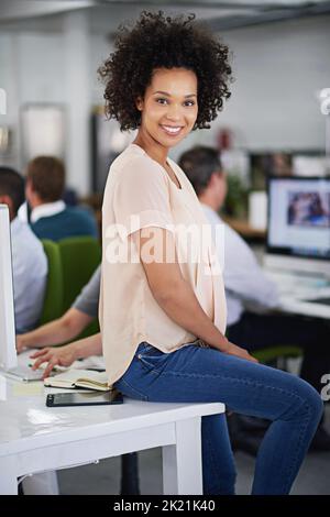 Shes a eu des affaires accumulen. Une jeune femme d'affaires attrayante assise sur son bureau avec quelques collègues en arrière-plan. Banque D'Images