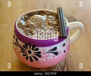 Chocolat chaud bouillant servi dans un mug décoratif rose et violet avec chocolat sur le dessus. Sur une table rustique en bois Banque D'Images
