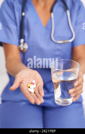 Prendre deux de ces quotidiennement avec de l'eau. Image rognée d'un médecin tenant des pilules et un verre d'eau Banque D'Images