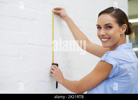 L'endroit parfait pour mon nouveau tableau. Une femme souriante prenant des mesures sur un mur Banque D'Images