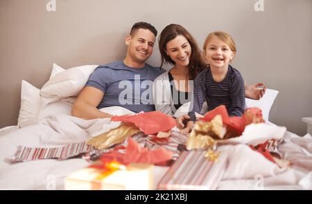 Tous mes cadeaux sont géniaux. Une petite fille recevant des cadeaux au lit de ses parents Banque D'Images