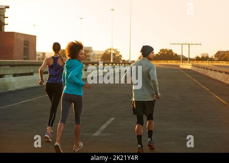 Ce tôt, c'est nous qui sommes propriétaires de la rue. Photo de trois jeunes joggeurs qui courent dans une rue vide à l'aube. Banque D'Images