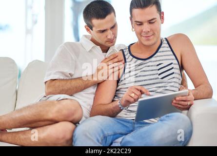 Prendre le plaisir dans les petits moments. Un couple gay utilisant une tablette numérique tout en se relaxant sur le canapé à la maison Banque D'Images