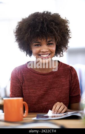 Une jeune femme attirante qui feuillit un magazine au bureau regorge d'idées brillantes Banque D'Images