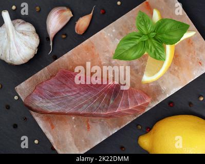 steak de thon cru sur pierre salée avec basilic, citron et ail sur fond d'ardoise noire, vue du dessus Banque D'Images
