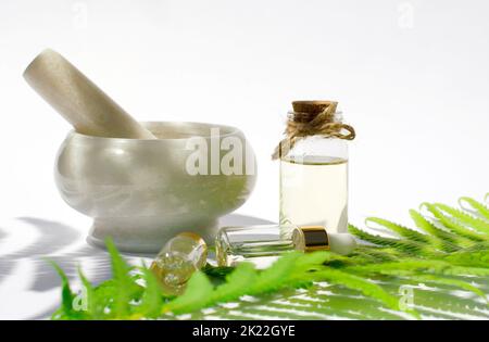Natural cosmetic. Essential oil made from natural ingredients. Bottles with essential oils, fern leaf and mortar with herbs on white background. Stock Photo