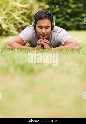 Pas un soin... un jeune homme allongé sur de l'herbe portant des écouteurs Banque D'Images