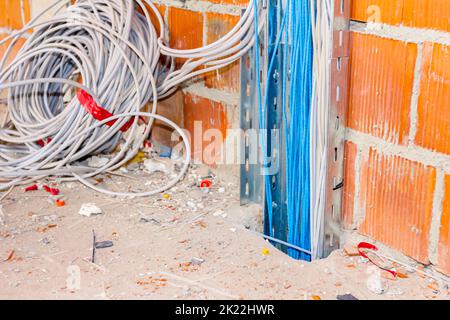 Un plateau perforé en métal avec faisceau de câbles isolés passe entre les sols à travers un trou quadratique au sol dans un bâtiment en construction. Banque D'Images